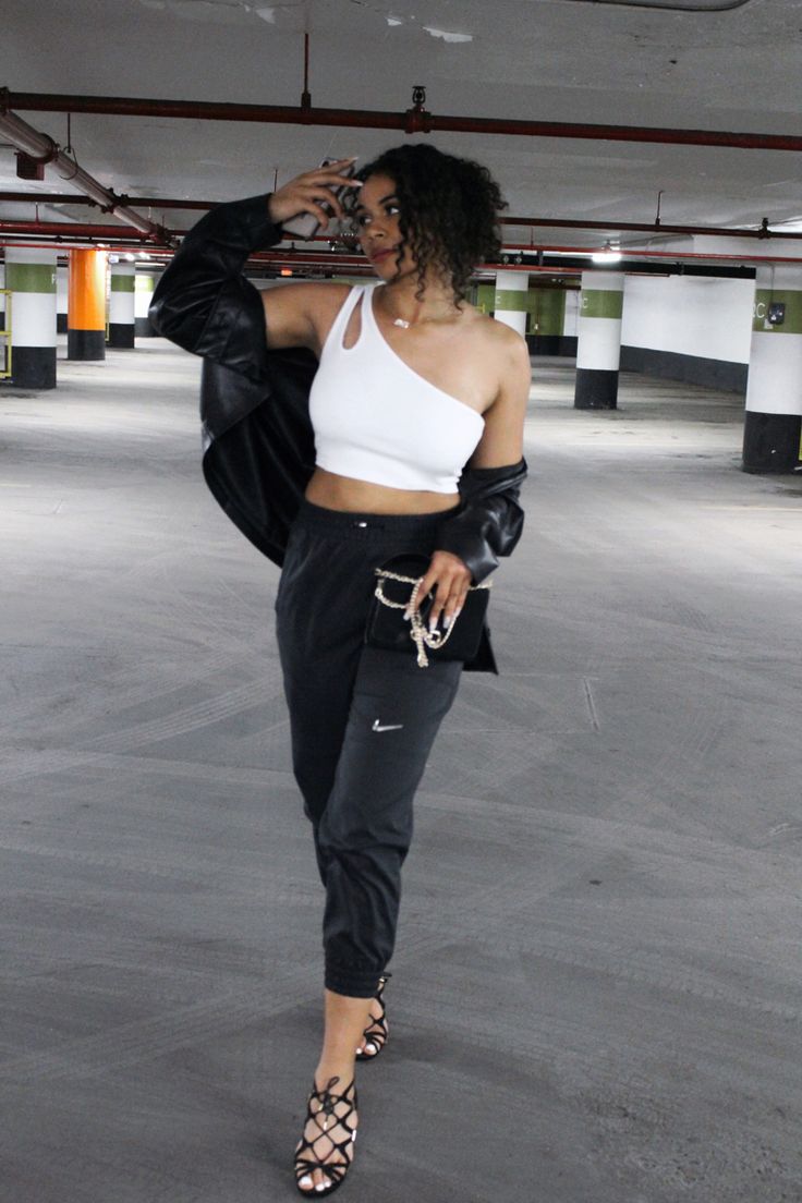 a woman in black and white is walking through an empty parking garage with her hand on her hip