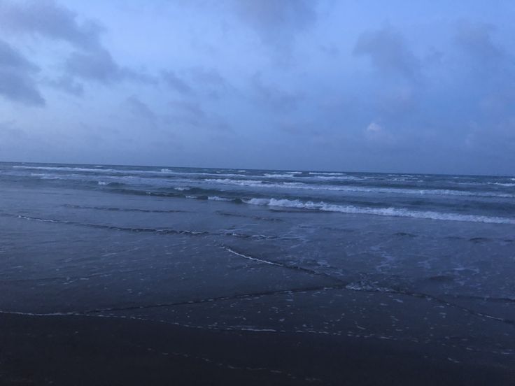 an ocean beach with waves coming in to shore and dark blue sky above the water