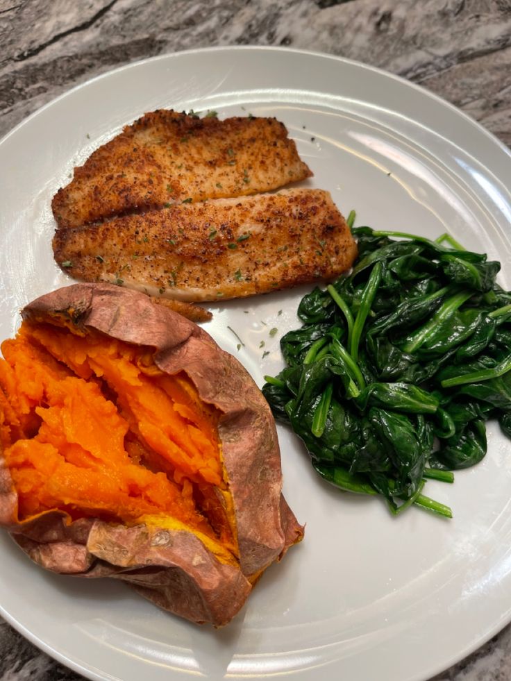 a white plate topped with meat and veggies on top of a marble counter