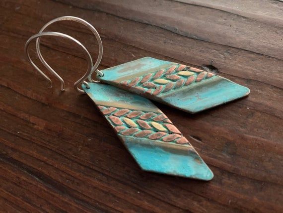 These earrings feature mixed metals of solid, gold brass & raw copper and are finished with a unique turquoise verdigris patina.  The patina has been sealed with a good coating of renaissance wax but should not be worn while showering or bathing to maintain patina.  The ear wires are forged by hand from 20g Sterling silver. These earrings have a celtic /  tribal feel.  They are versatile and suitable for just about any style, from modern to rustic. They're substantial but comfortable to wear Artisan Turquoise Brass Jewelry, Rustic Copper Jewelry For Festivals, Artisan Turquoise Metal Earrings, Turquoise Brass Jewelry For Festivals, Blue Metal Jewelry With Patina, Blue Hammered Artisan Jewelry, Unique Turquoise Copper Jewelry, Gold Dangle Jewelry With Patina, Artisan Blue Hammered Jewelry