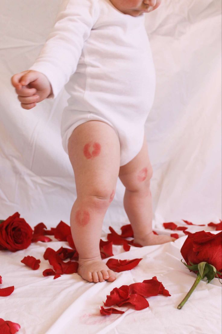 a baby in white bodysuit standing on rose petals