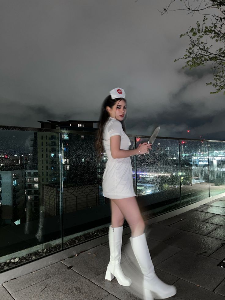 a woman in white dress and knee high boots standing next to a fence at night