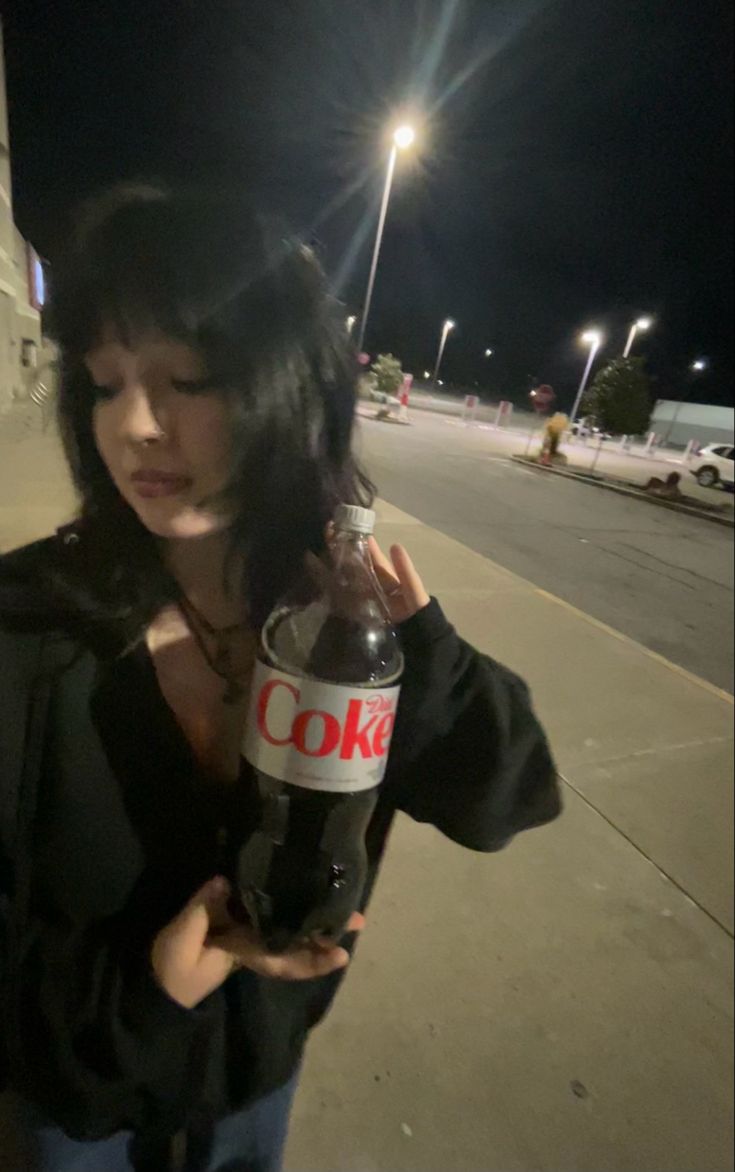 a woman standing on the sidewalk holding a coke bottle