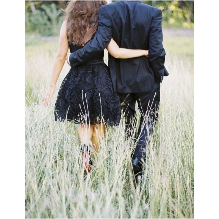 black and white photograph of two people walking through tall grass in an open field, one holding the other's back