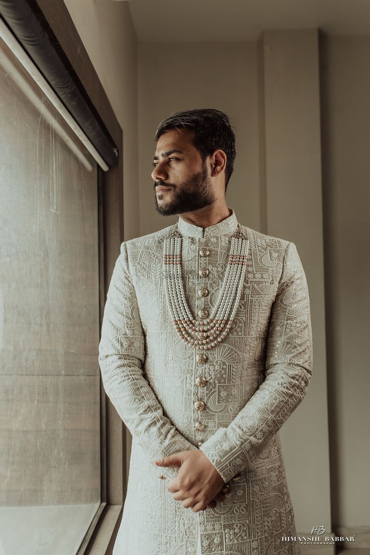 a man standing in front of a window wearing a white sherve with beads on it