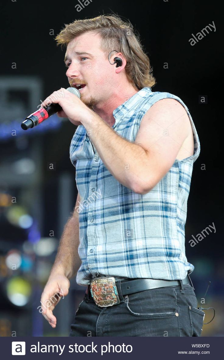 a man with ear buds on his ears singing into a microphone at an outdoor concert - stock image