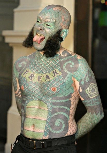 a man with tattoos on his body and face is standing in front of a building