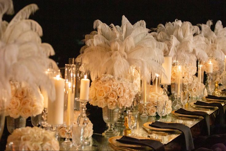 a long table with white flowers, candles and feathers on it is set up for a formal function