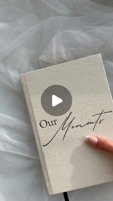 a hand holding a book with the words our moments written on it and a video playing button