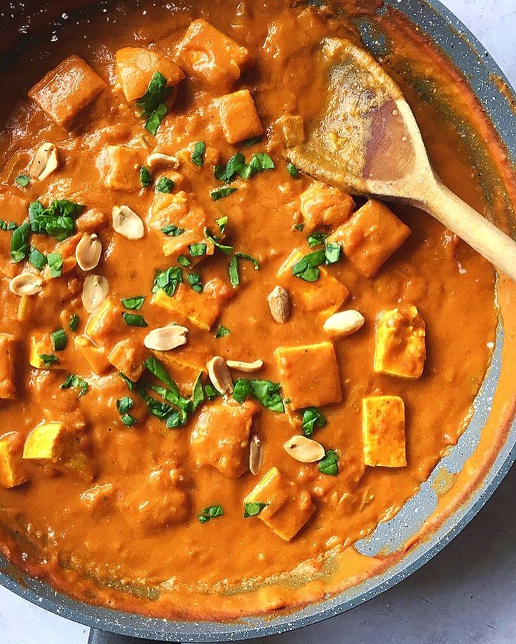 a pan filled with tofu and cashews next to a wooden spoon