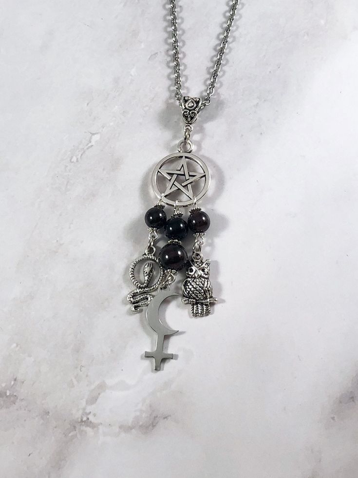 This beautiful chain necklace is the perfect way to express your affinity for Lilith. Charms: Snake Astrological Symbol Owl 3 garnet beads and one onyx bead also make up the pendant. Your choice of top charm: Pentacle, Chandelier, or Triple Moon Available in a variety of lengths. Secured with a lobster clasp. Chain is stainless steel. Charms are zinc alloy. All materials are lead and nickel free. Comes in a jewelry box so it's ready to be given as a gift. Have a idea for a custom order? I'd love Symbolic Black Necklace With Adjustable Chain, Black Pendant Charm Necklace With Chain, Spiritual Black Chain Necklaces, Black Spiritual Chain Necklace, Spiritual Black Chain Necklace, Spiritual Black Dangle Necklaces, Black Dangle Necklace With Lobster Clasp, Black Jewelry With Dangling Charms For Gift, Black Metal Pendant Charm Necklace