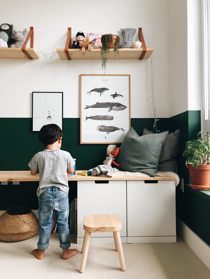 a young boy standing in front of a desk with books and toys on top of it