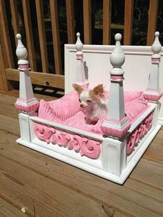 a small dog is sitting in a bed made out of pink and white furniture on a wooden deck