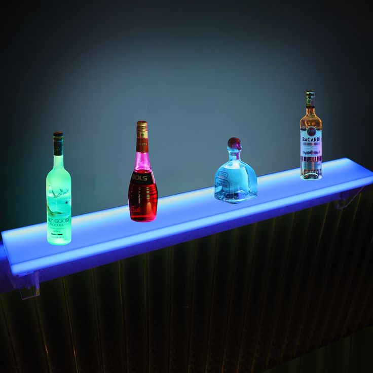 three bottles are lined up on a shelf with neon lights in the dark behind them