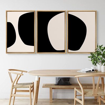 two black and white paintings hanging on the wall above a dining room table with chairs