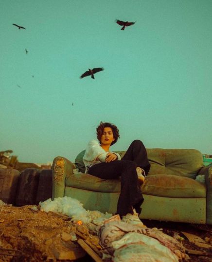 a woman sitting on top of a green couch next to birds flying over the ground