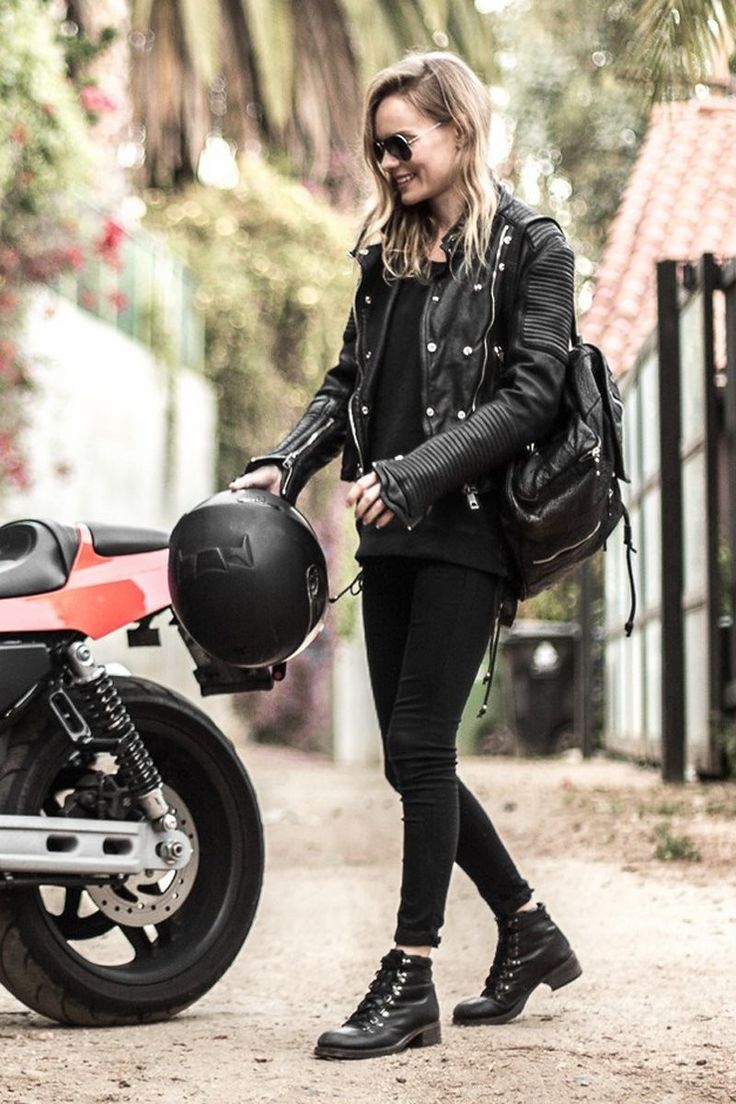 a woman in black is walking next to a motorcycle