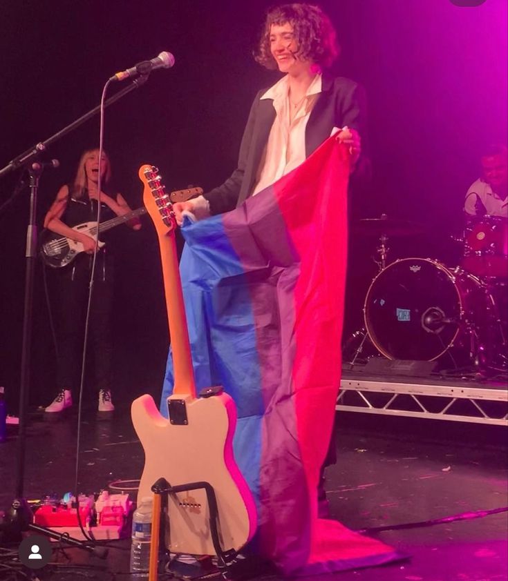 a person holding a guitar on stage with other people in the background