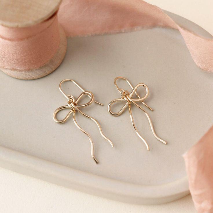 delicate 14k gold fill bow earring hand made by Token Jewelry, photographed on a ceramic dish with a light pink ribbon Bow Earrings Diy, Coquette Earrings, Bow Earring, Wire Earrings Handmade, Bracelet Inspo, Ultra Feminine, Bow Jewelry, Coquette Bow, Handmade Beaded Jewelry