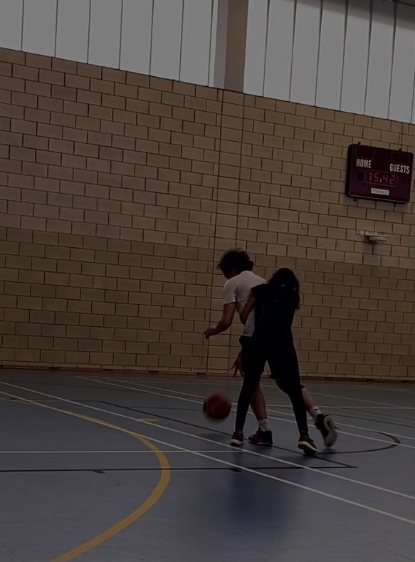 two people are playing basketball on an indoor court with brick walls and yellow lines around them