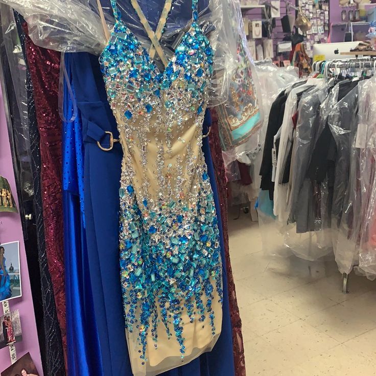 This Gown Is A Faviana With Blue And Clear Stones All Over The Dress And With Crisscross Straps In The Back. Blue Rhinestone Gown For Prom Season, Glamorous Blue Rhinestone Dress, Fitted Blue Gown With Rhinestones, Blue Fitted Gown With Rhinestones, Embellished Royal Blue Dress For Gala, Embellished Light Blue Dress For Prom Season, Embellished Blue Dresses For Prom Season, Blue Embellished Dress For Prom Season, Light Blue Embellished Floor-length Dress