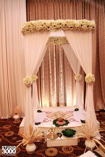 a decorated bed with white drapes and flowers on the headboard for a wedding ceremony