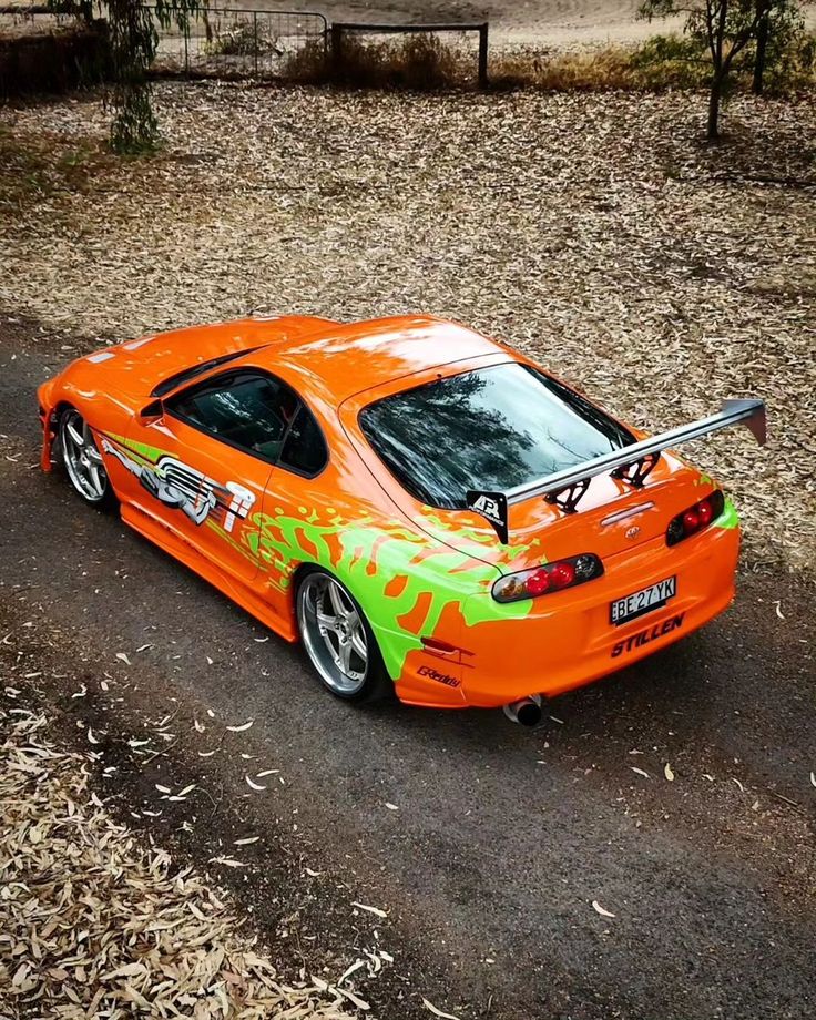 an orange and green car parked on the side of a road next to some trees