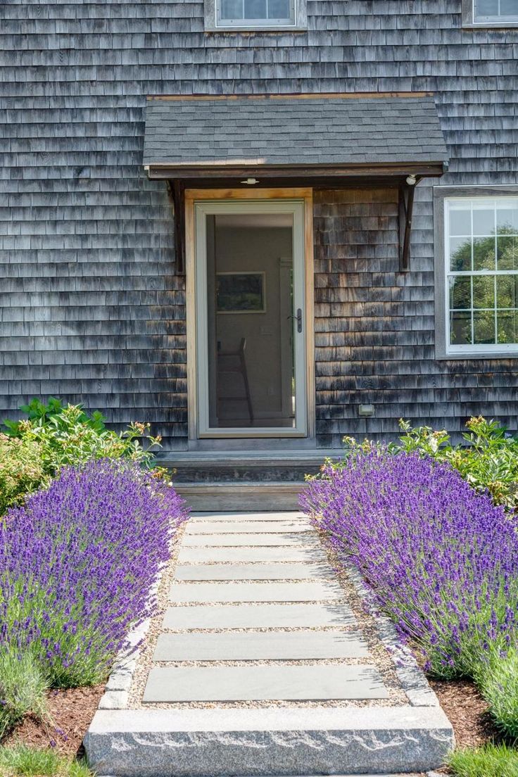 a house with lavender flowers in front of it and a stone walkway leading to the door