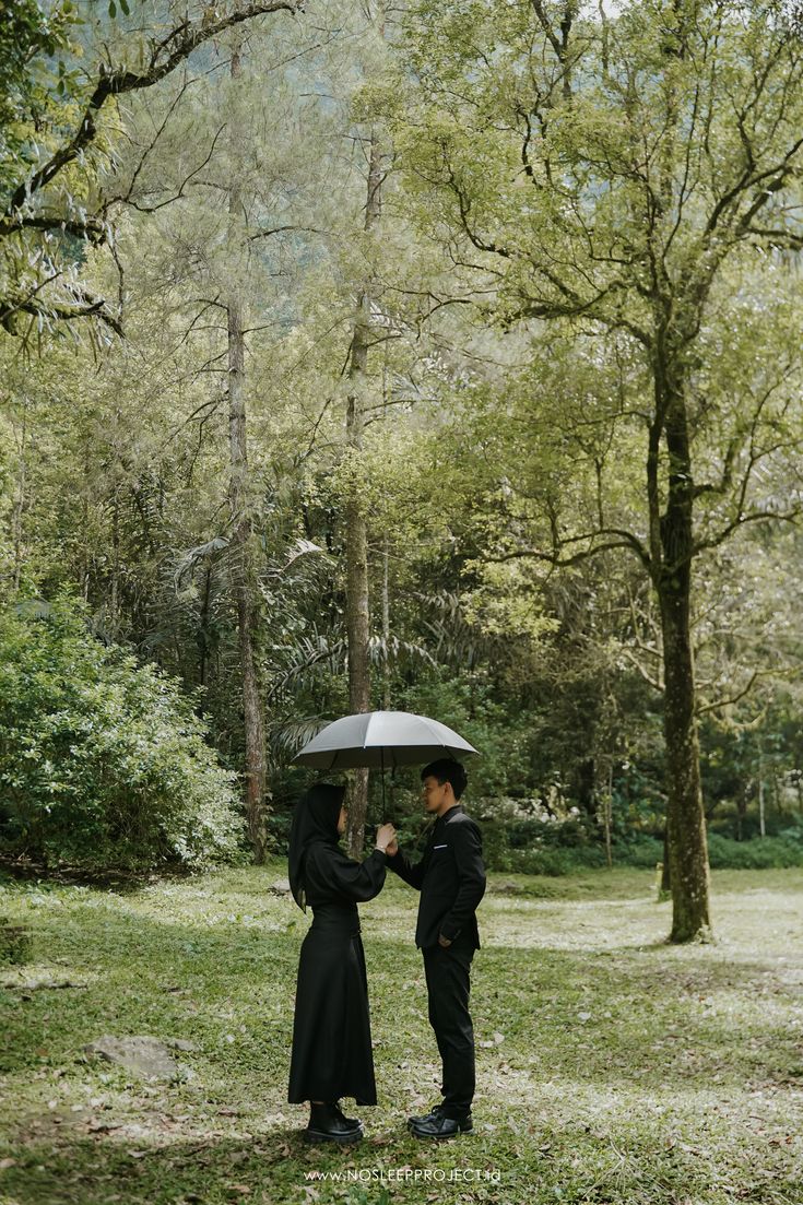 two people standing in the grass holding an umbrella over their heads and facing each other