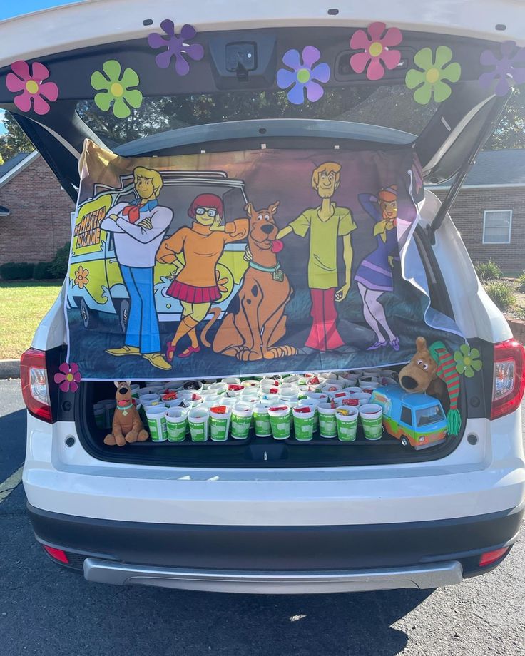 the back end of a white car with cartoon characters on it and cupcakes in front