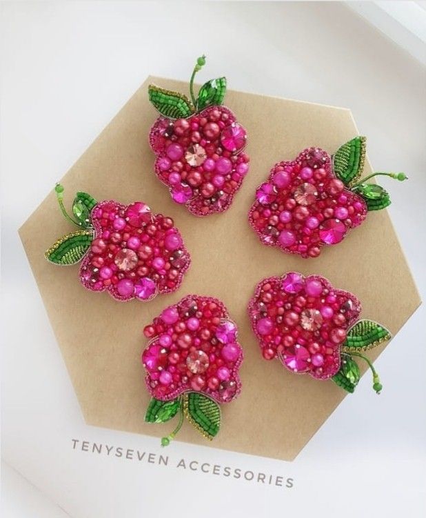 four pink beaded flowers sitting on top of a piece of paper with green leaves