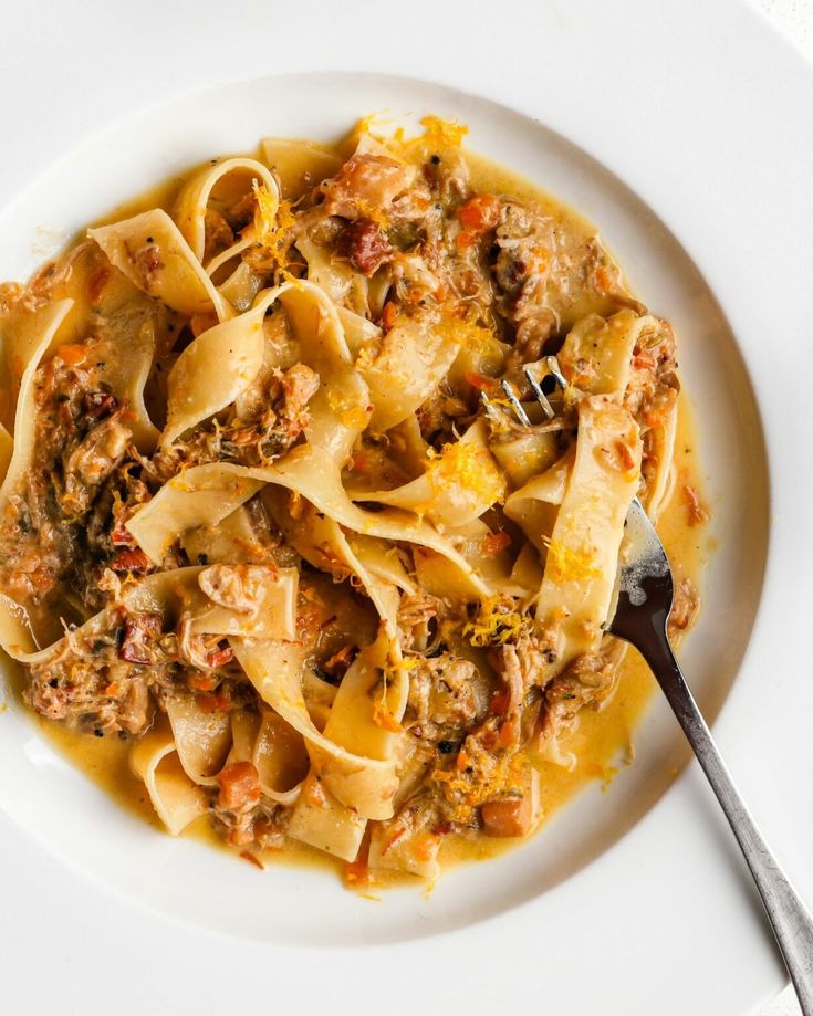 a white plate topped with pasta covered in meat and sauce next to a silver fork