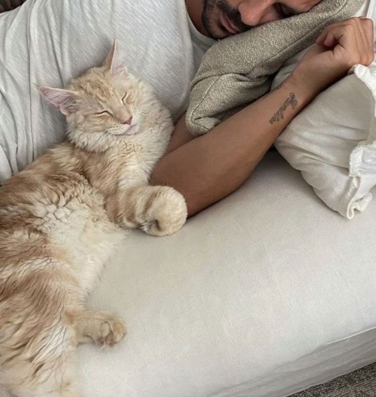 a man laying on top of a white couch next to a cat