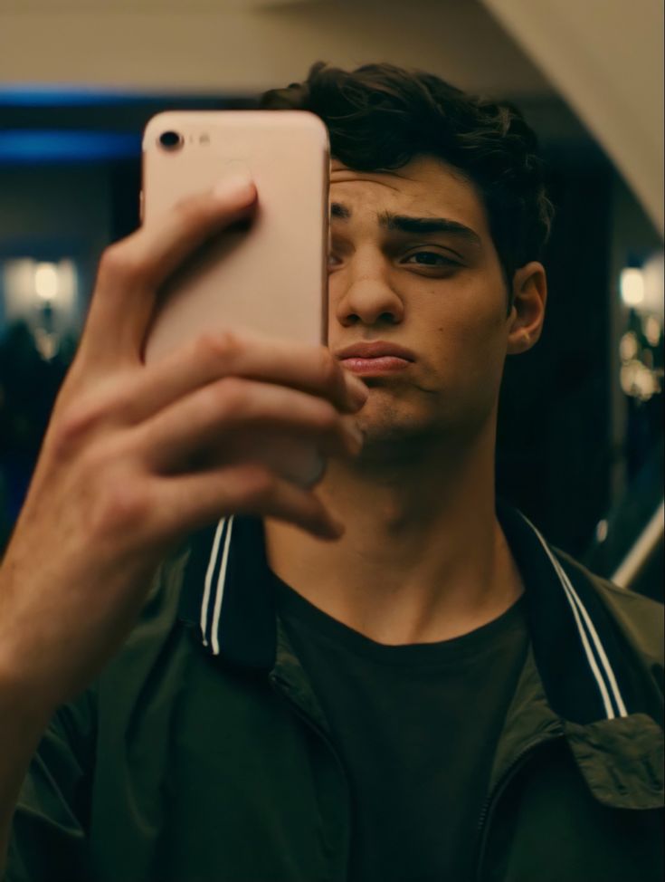 a young man taking a selfie with his cell phone in front of him and looking at the camera