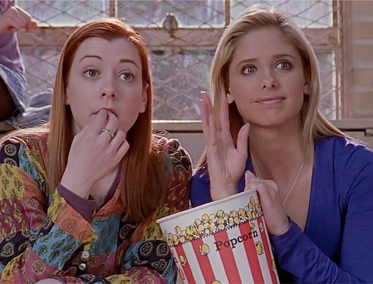 two women sitting next to each other with popcorn in front of their faces and one holding her hand up