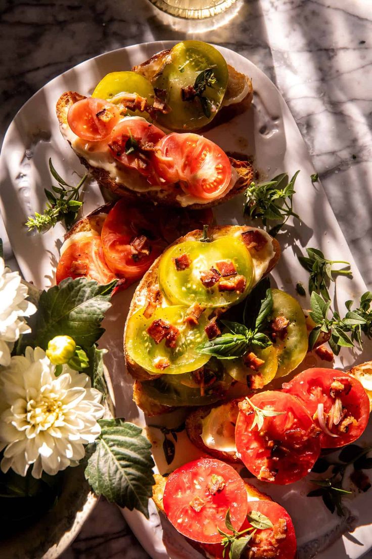 tomatoes and other vegetables on a white plate with flowers next to it in the sun