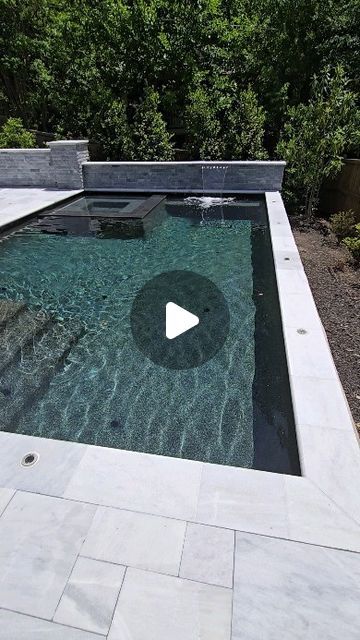 an outdoor pool with a stone patio and water feature in the middle, surrounded by greenery