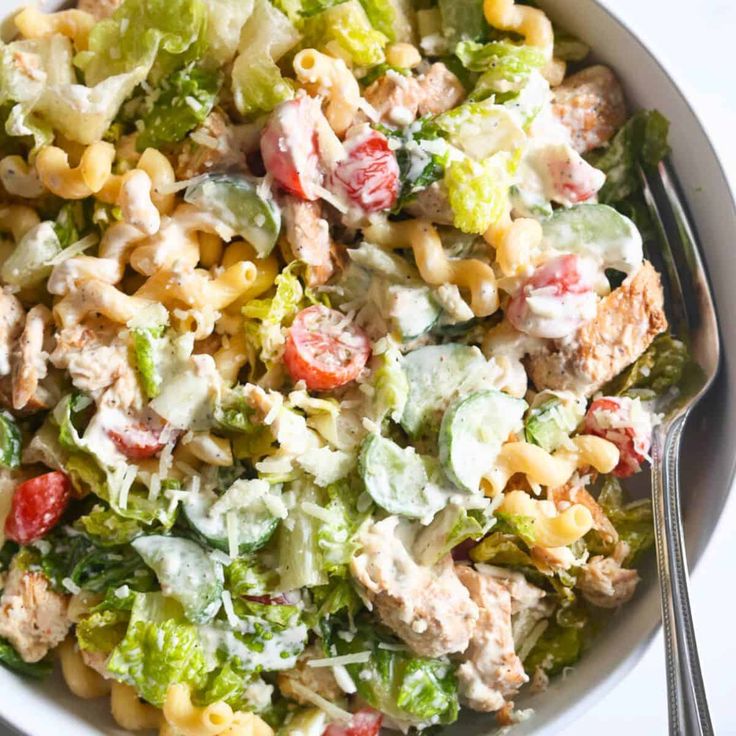 a white bowl filled with pasta salad on top of a table next to a fork