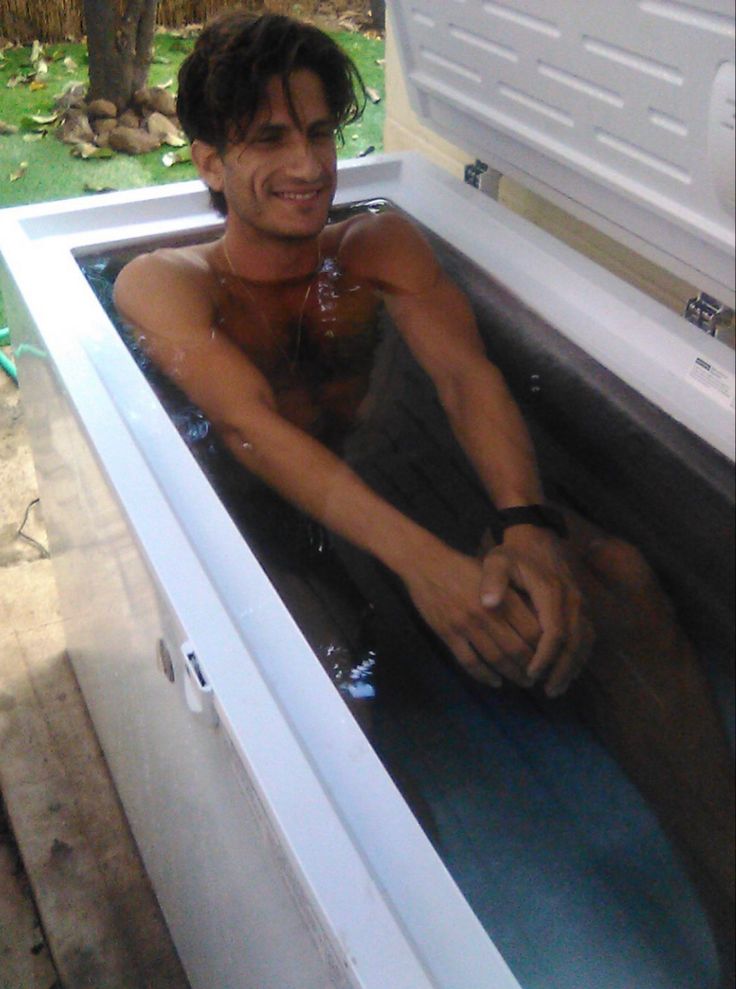 a man sitting in the back of an open white chest freezer filled with water