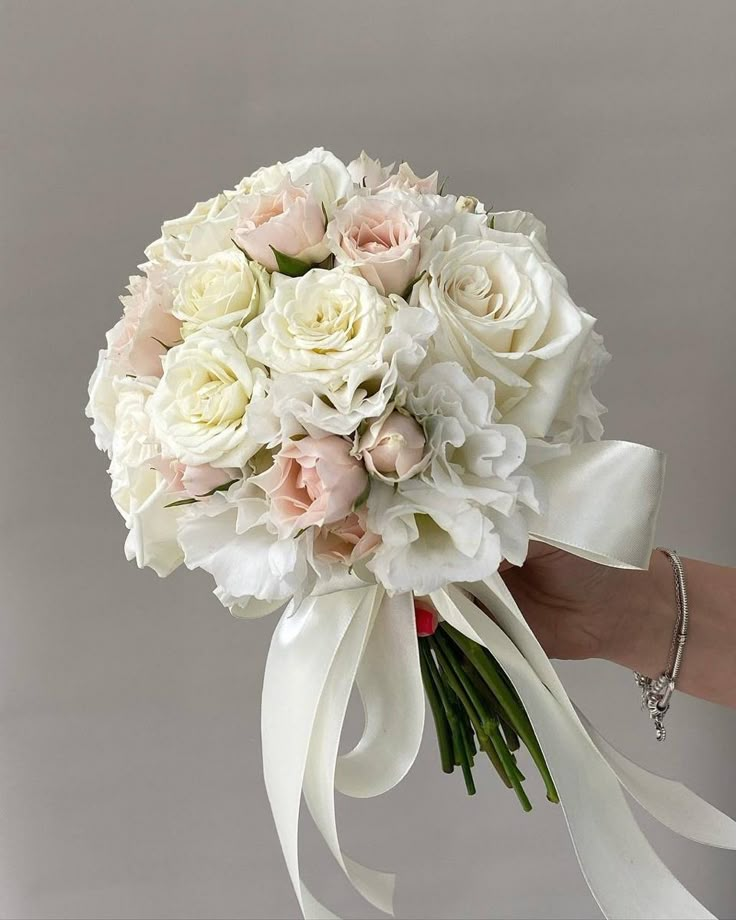 a bride's bouquet with white and pink flowers is being held by her hand