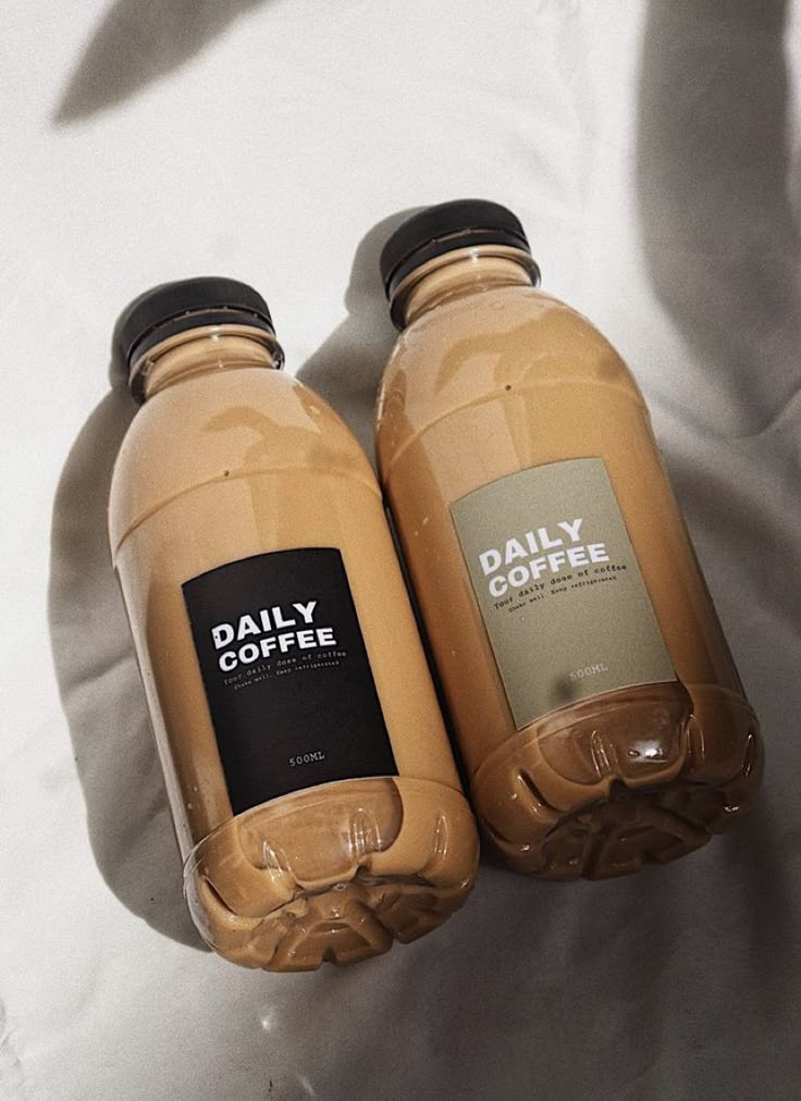 two bottles of coffee sitting next to each other on a white cloth covered bed sheet