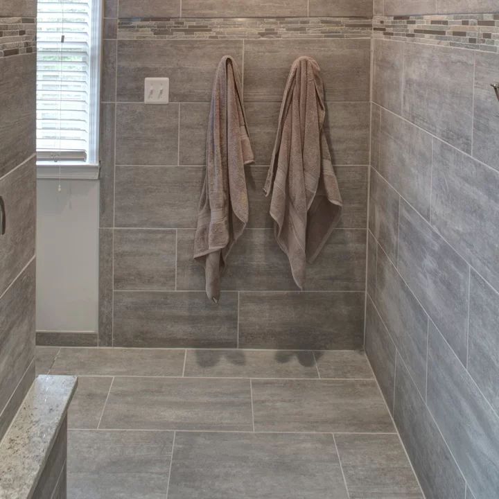 two towels hanging on the side of a shower wall next to a window with shutters