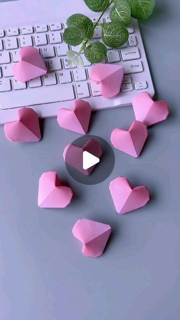 pink paper hearts sitting on top of a computer keyboard next to a green leafy plant