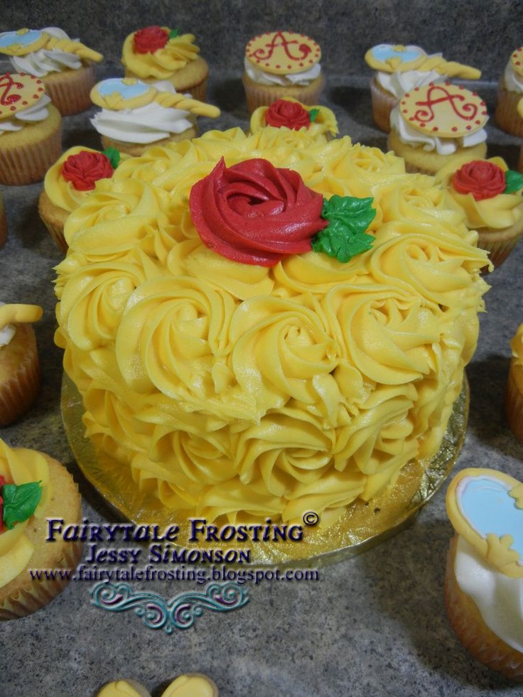 there is a cake with yellow frosting and red rose on top, surrounded by other cupcakes