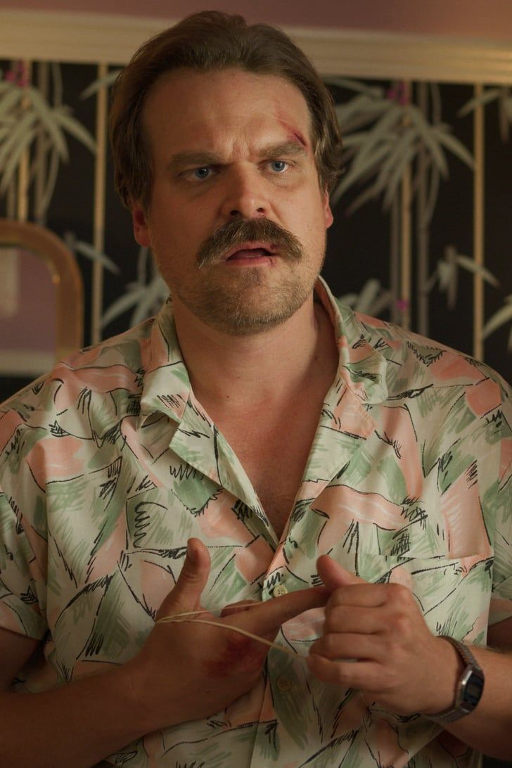 a man in a hawaiian shirt is holding something up to his chest and looking at the camera