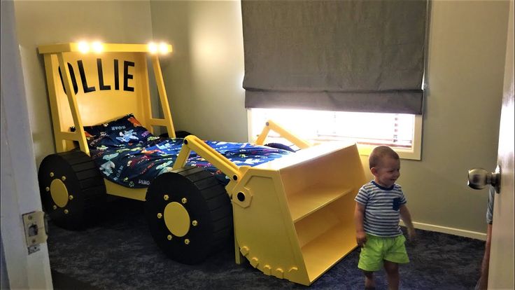 a toddler standing in front of a bed made to look like a bulldozer