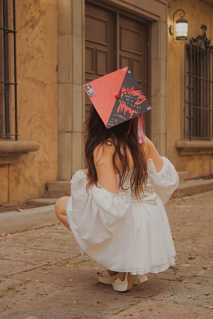 a woman in a white dress is wearing a red and black hat on her head