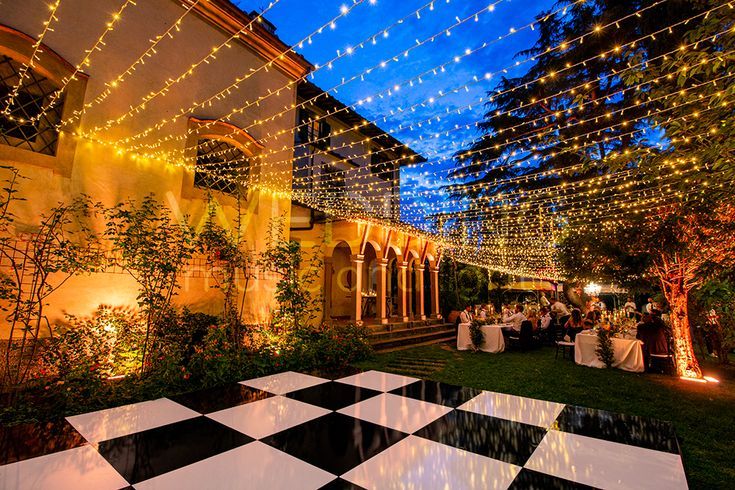 an outdoor party with lights strung from the ceiling and decorations on the ground, in front of a building