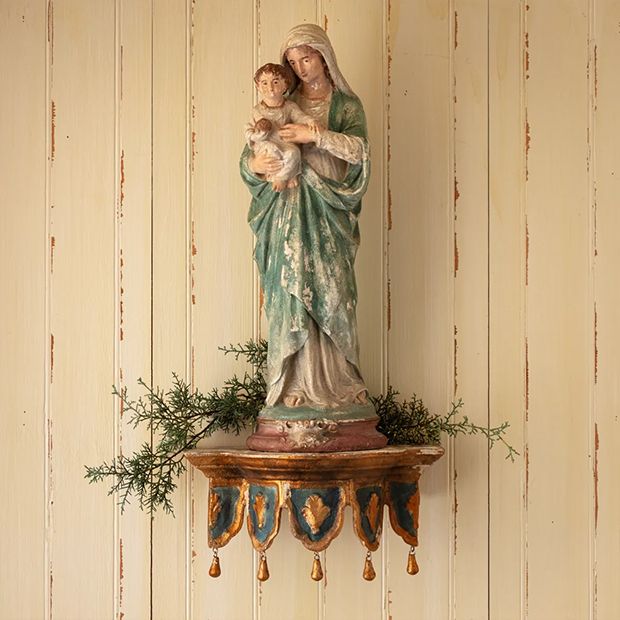 a statue of a woman holding a child on top of a wooden table next to a wall