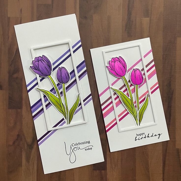 two cards with purple flowers on them sitting on a wooden table next to each other